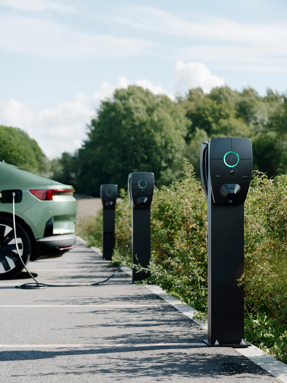 Oszlopos autótöltők egy kültéri parkolóban, egy autó éppen tölt